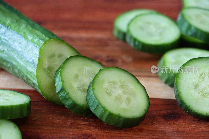 全画幅的黄瓜(Cucumis sativus)在木制砧板上，半水果和切片显示绿色的皮，白色的肉和白色的种子，木纹背景，重点在前景